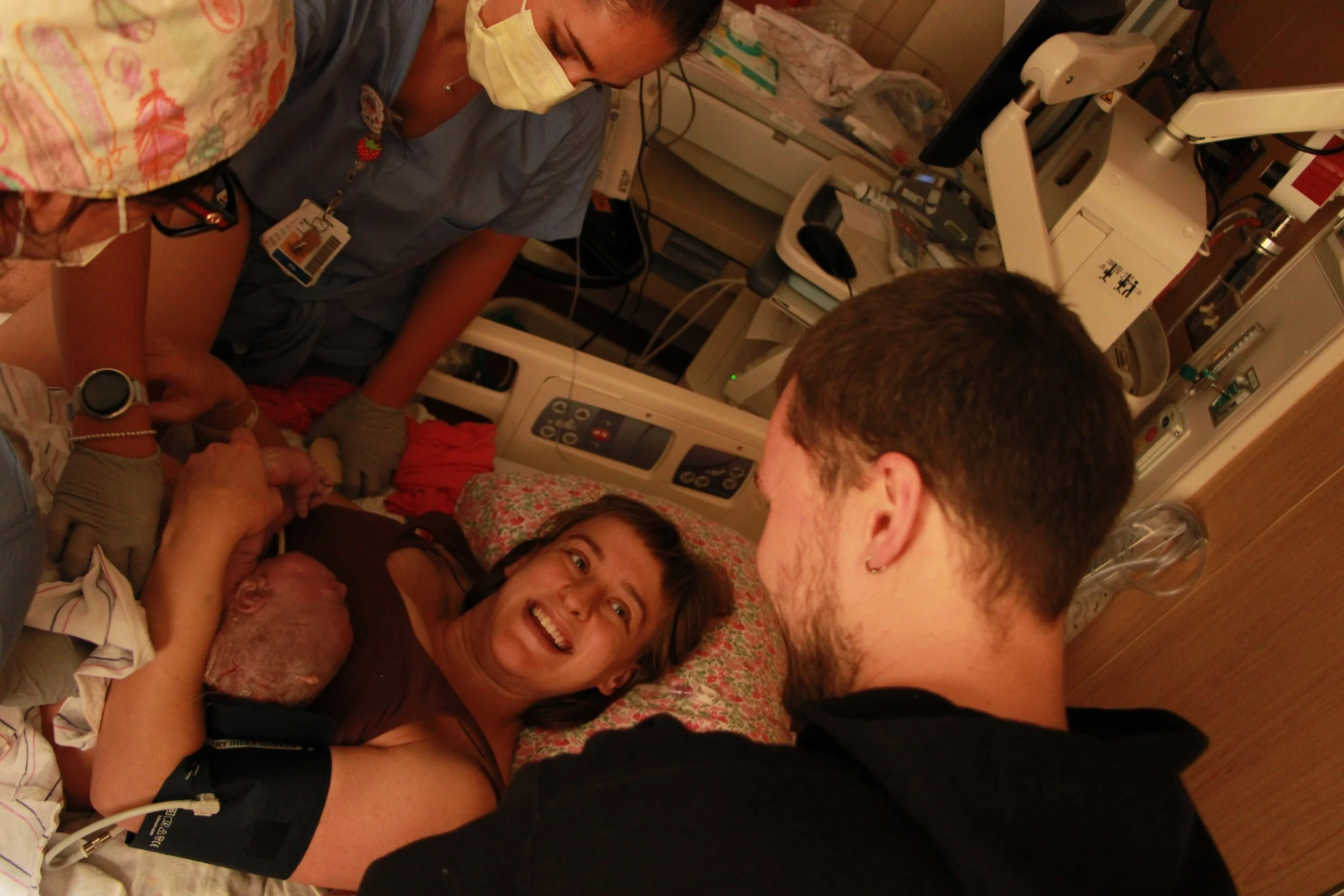 Parents and medical staff celebrate beside a newborn baby in a hospital delivery room.
