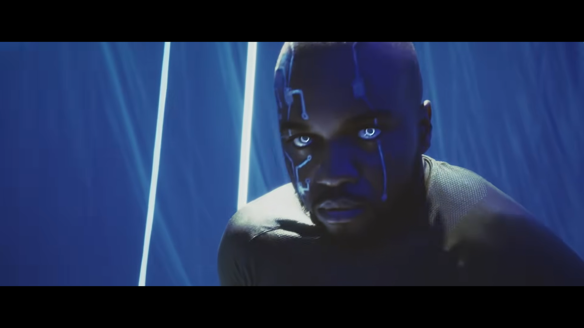 Un homme avec un visage marqué par des lignes lumineuses bleues, regardant fixement la caméra dans une ambiance sombre et lumineuse avec des rayons lumineux bleus.