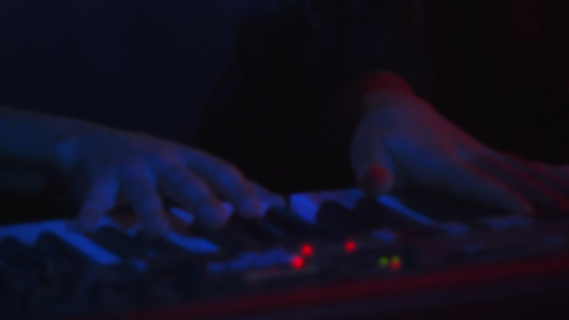 Une personne jouant du piano dans un environnement sombre, éclairée par des lumières rouges et bleues.
