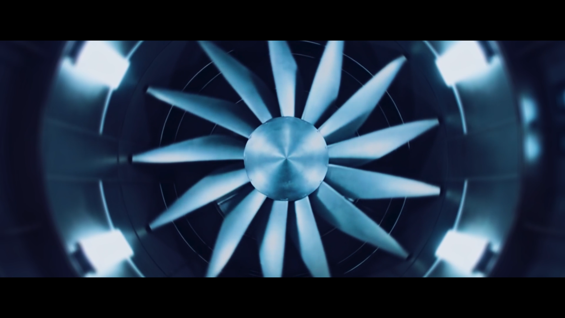 Une vue artistique d'une turbine d'avion en acier, vue du dessous, avec des pales éclairées en bleu dans un environnement sombre.