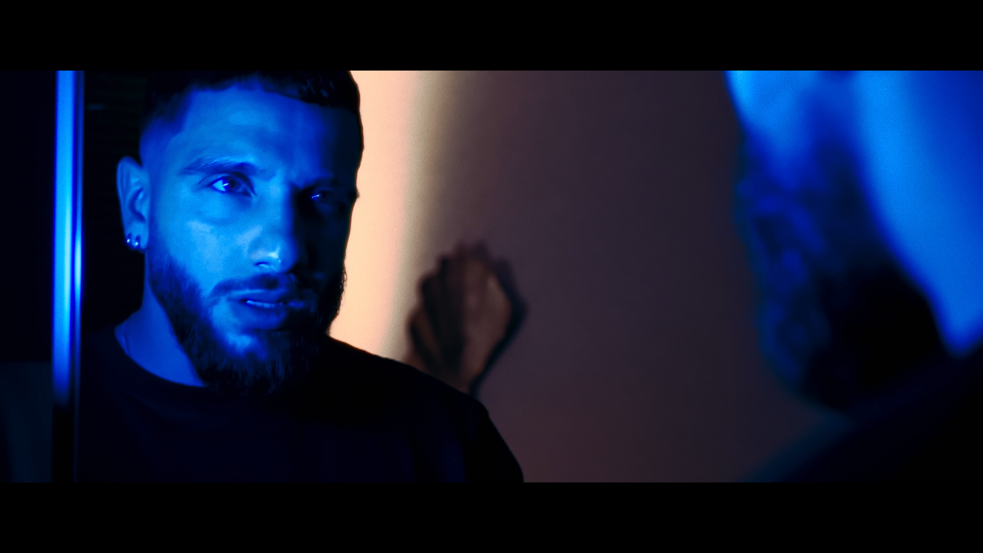 Jeune homme regardant un miroir avec un éclairage bleu, face à lui, avec un fond sombre.