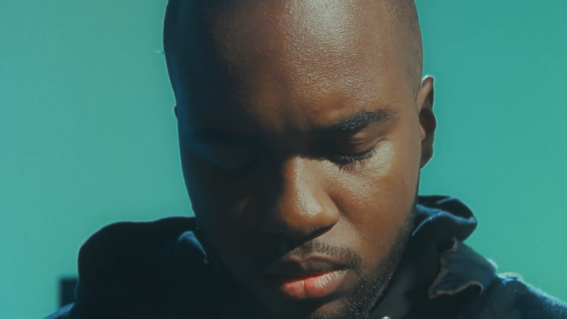 Un homme avec la tête inclinée et les yeux fermés, fond vert.