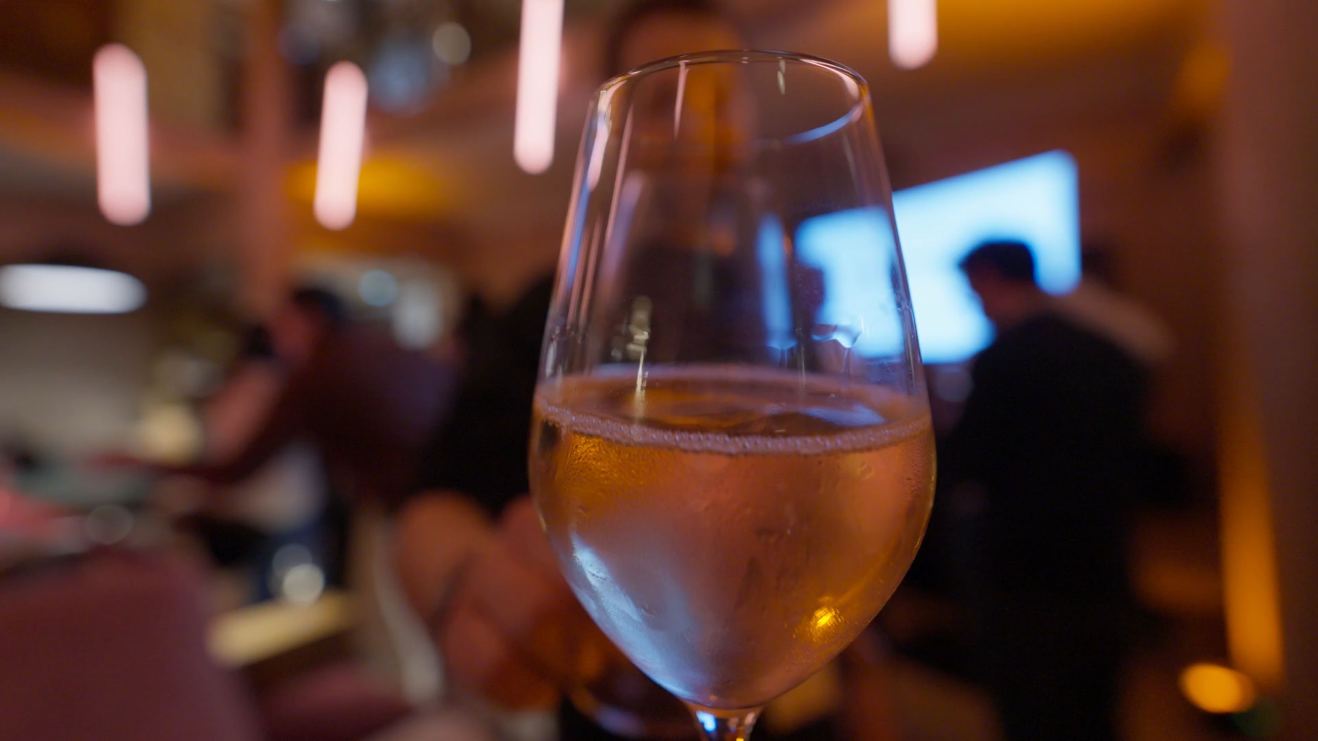 Verre de vin rosé dans une ambiance de restaurant ou bar, flou d'arrière-plan avec des personnes et de la lumière tamisée.