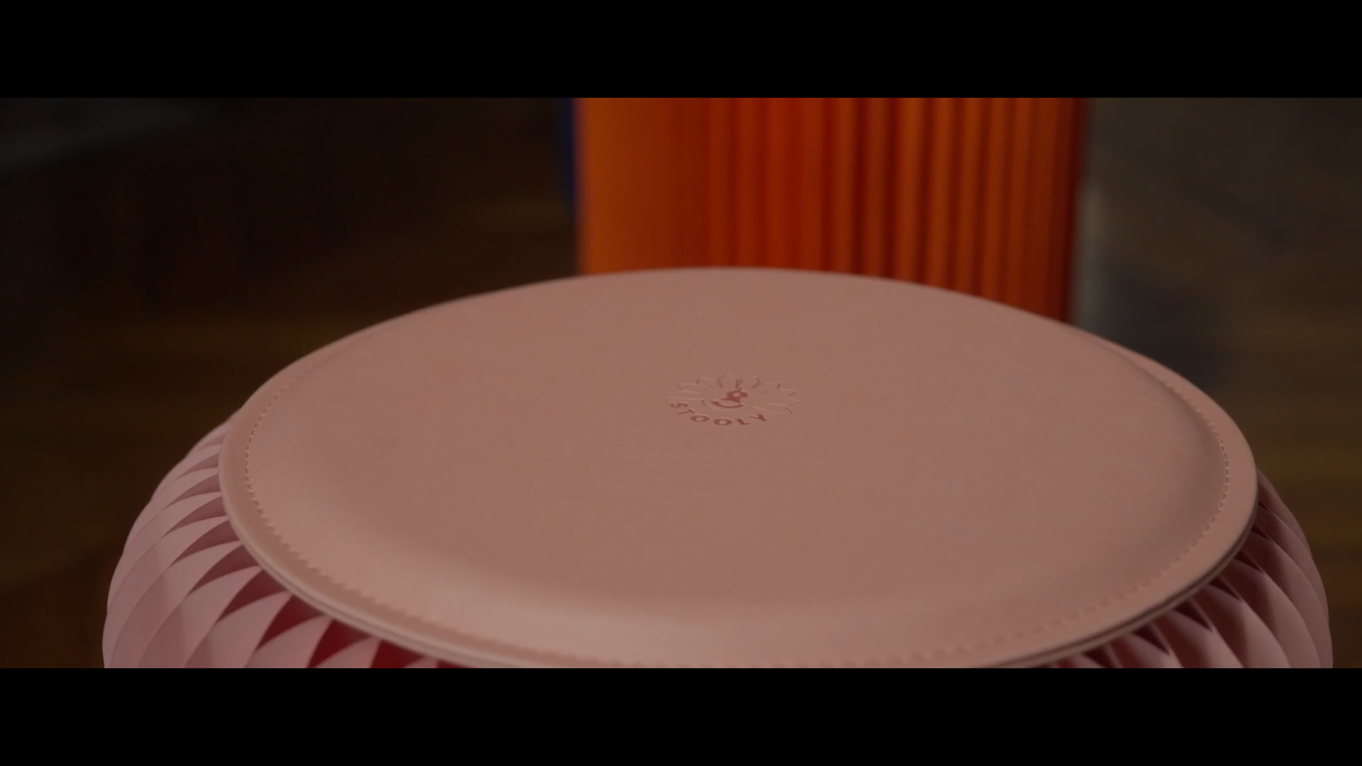 Une enceinte en forme de ballon de football rose avec un motif en zigzag. Sur le dessus, il y a un logo rouge avec une icône de haut-parleur.