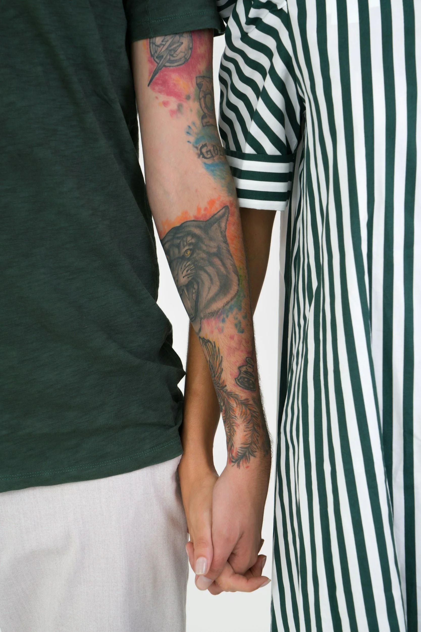 A couple holding hands, with visible tattoos on their arms, wearing casual clothing.