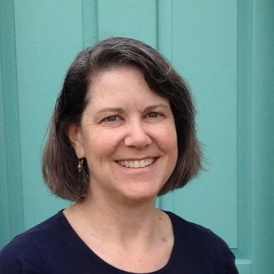 A woman with short dark hair smiling in front of a teal-colored door.
