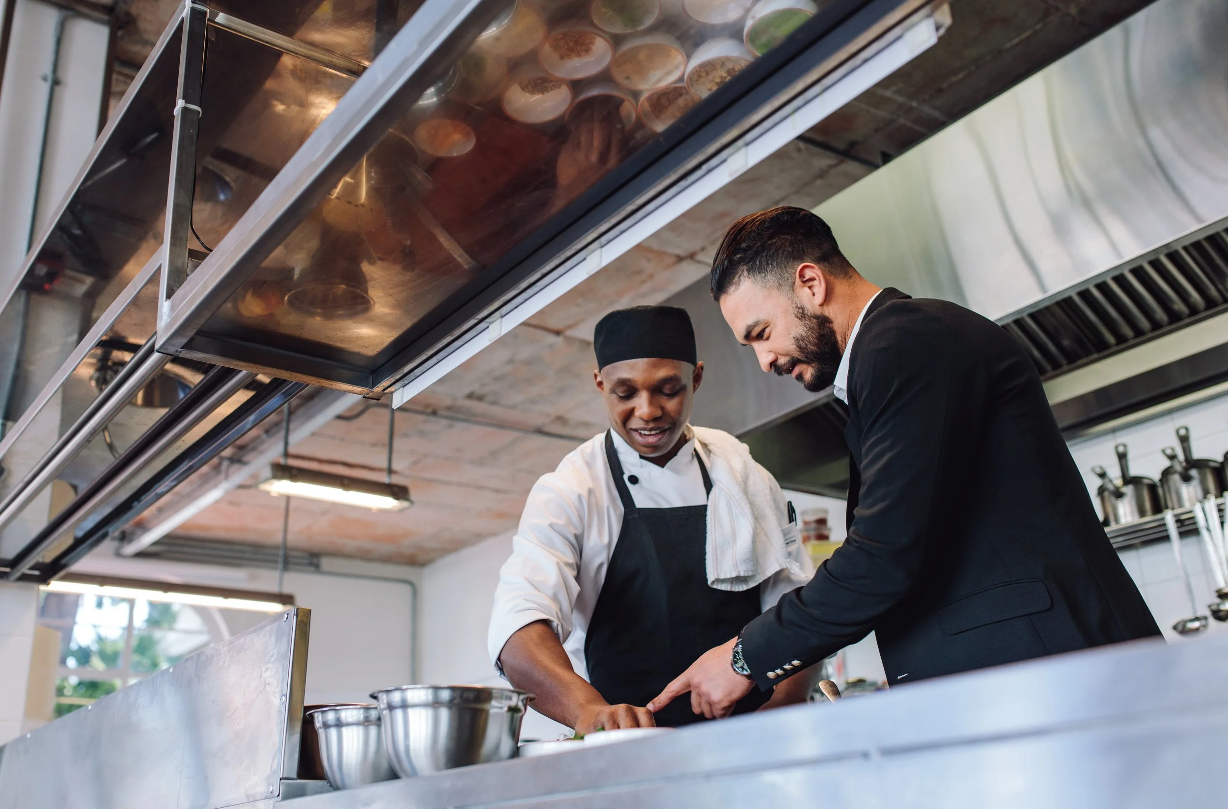 A chef and a man in a suit preparing food together in an industrial test kitchen.