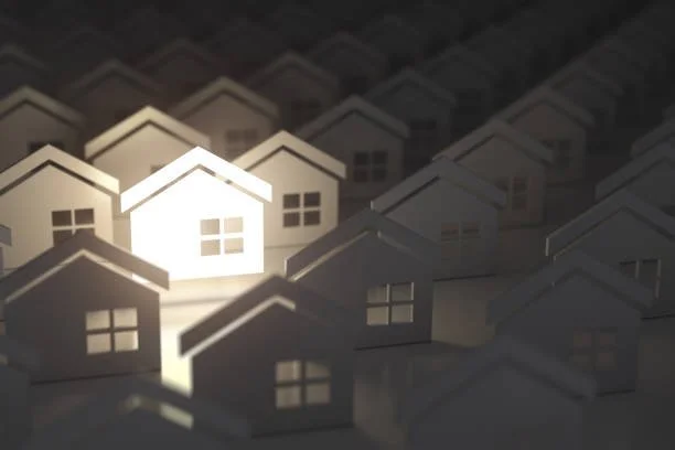 A collection of small paper house models with one house illuminated, symbolizing real estate or housing market.