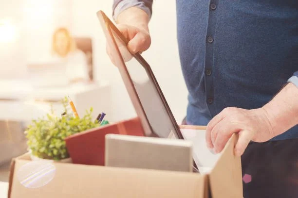 Person reaching into a cardboard box filled with office supplies and electronic devices.