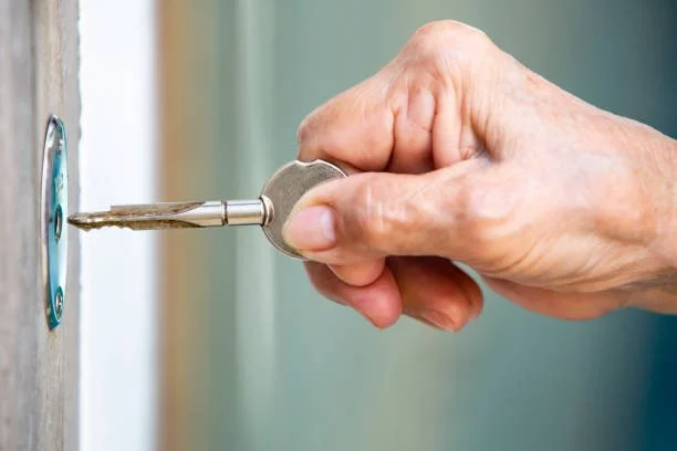 Close-up of an elderly person's hand inserting a key into a door lock.