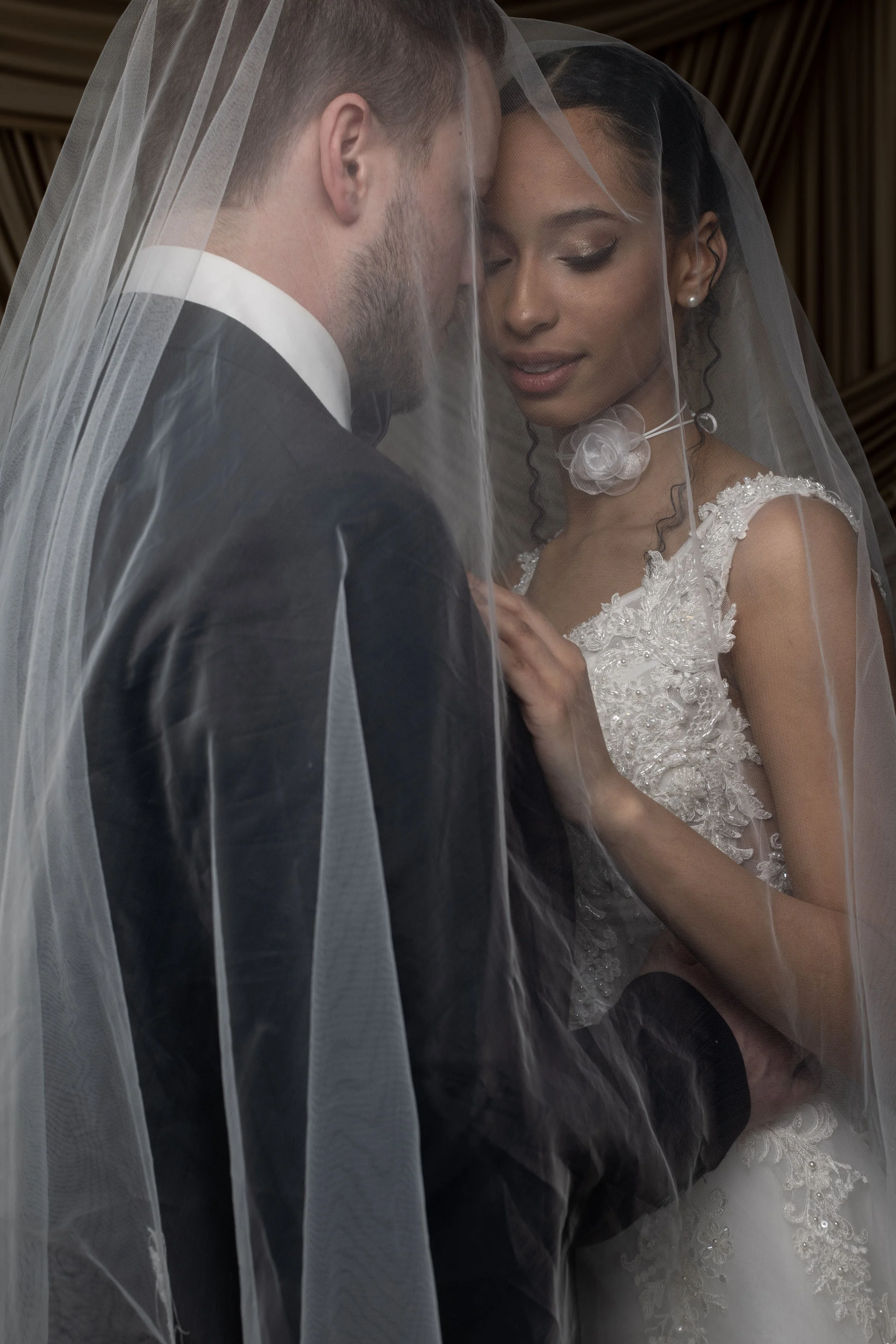 Bride and groom under a veil, close-up portrait on their wedding day.
