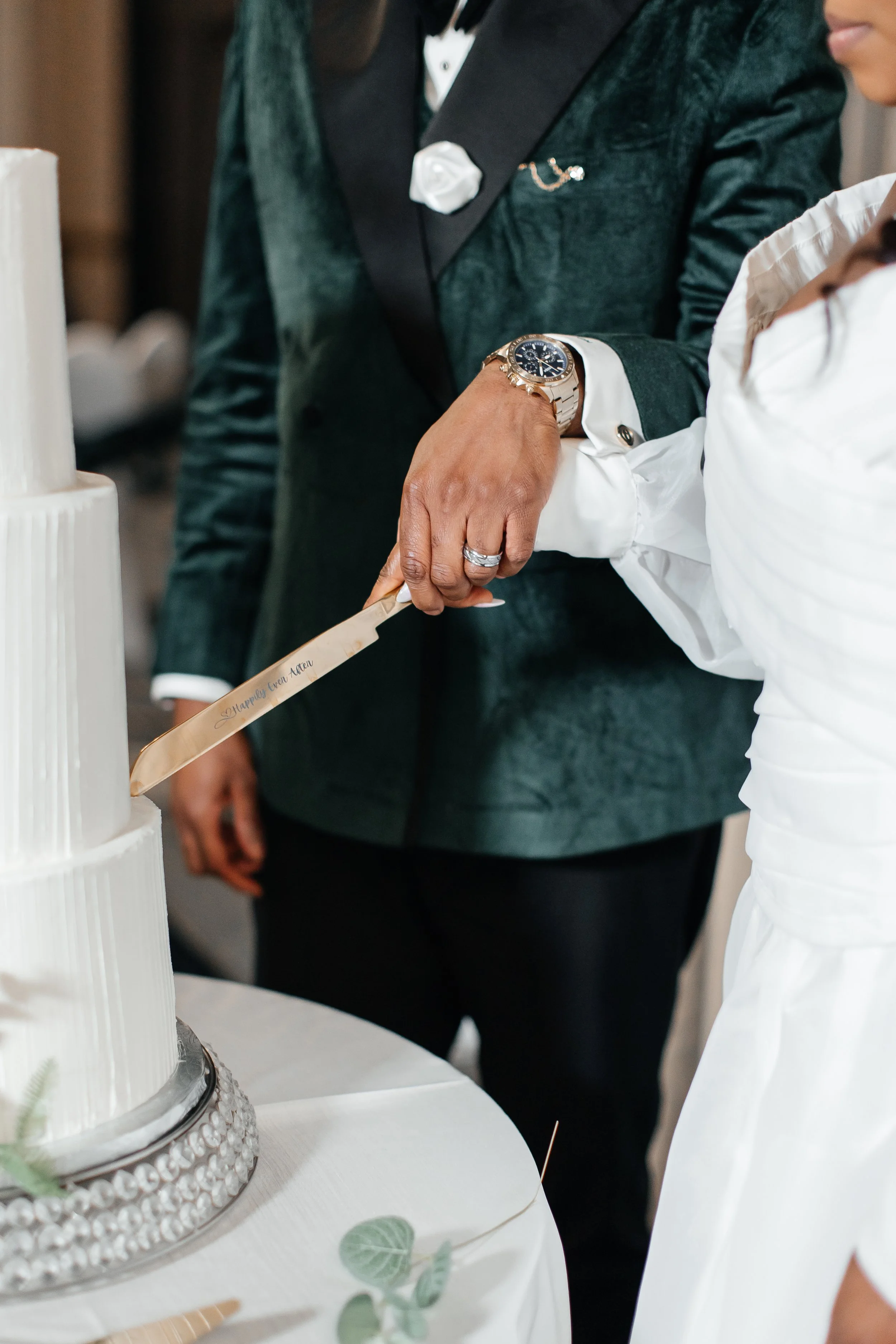 Couple cutting a wedding cake together with a knife that says 'Happily Ever After' in an elegant setting.