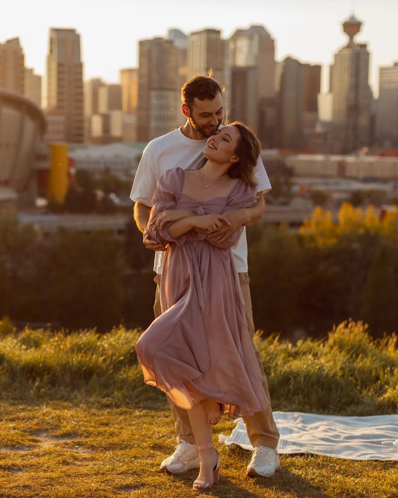 A couple dancing outdoors at sunset with a city skyline in the background.
