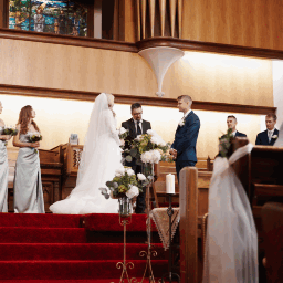 A wedding ceremony inside a church with a bride and groom exchanging vows, surrounded by bridesmaids and groomsmen.