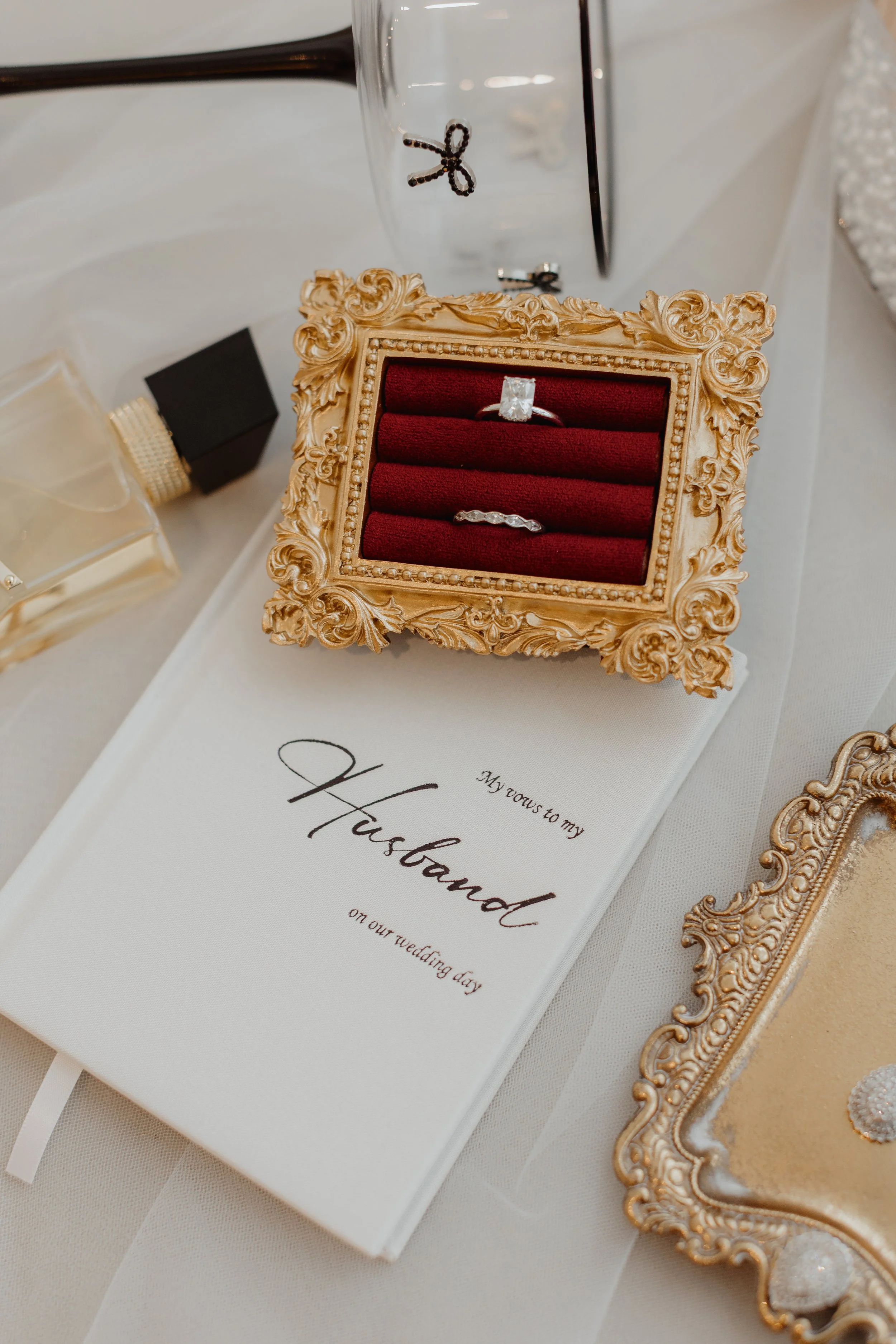 A wedding ring set with an engagement ring and wedding band in a decorative gold box with a red interior, placed on a white wedding program that reads 'My vows to my Husband on our wedding day'.