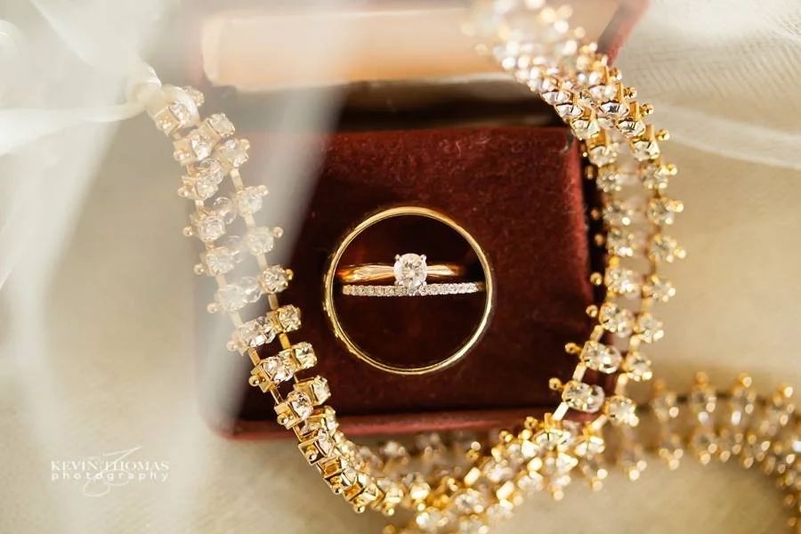 A gold ring with a diamond in a jewelry box surrounded by a gold chain with diamonds.