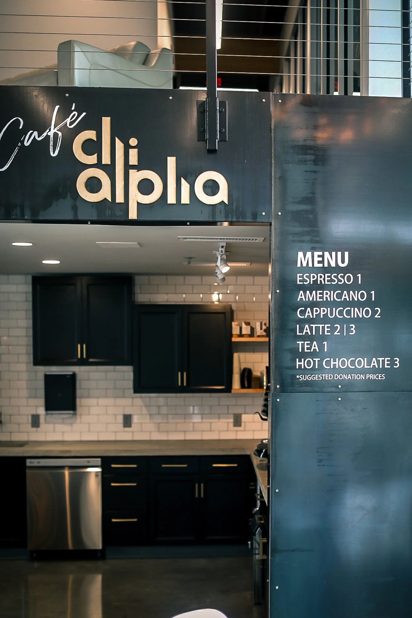Interior of a modern coffee shop with black cabinets and a menu board listing various coffee drinks and prices.