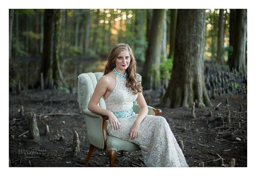 A woman in a white lace dress sitting on a vintage armchair outdoors in a forest setting.