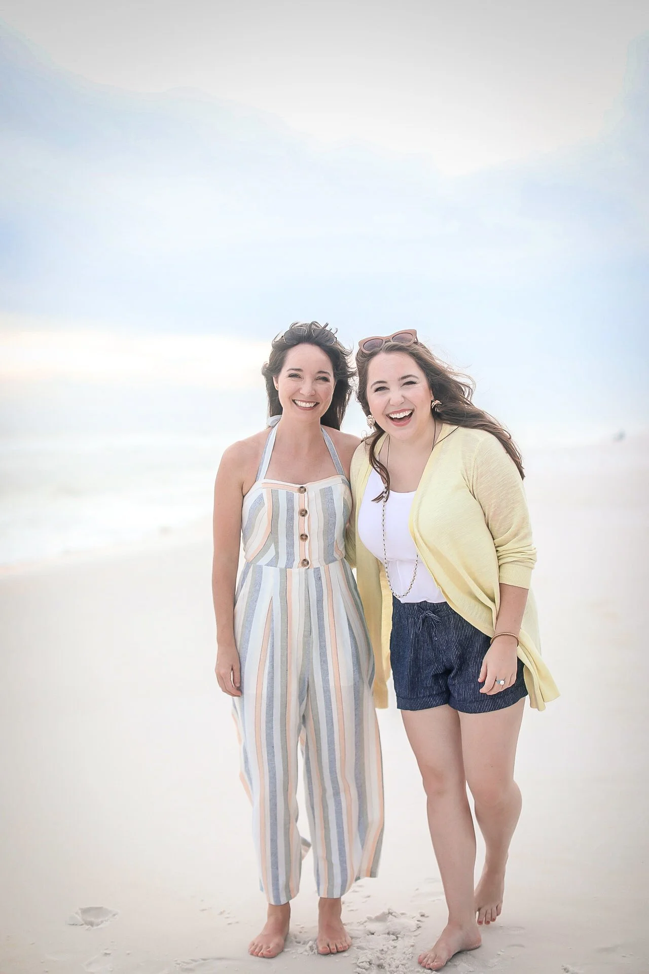 Two women standing on the beach, smiling and enjoying the day, with ocean and sky background.
