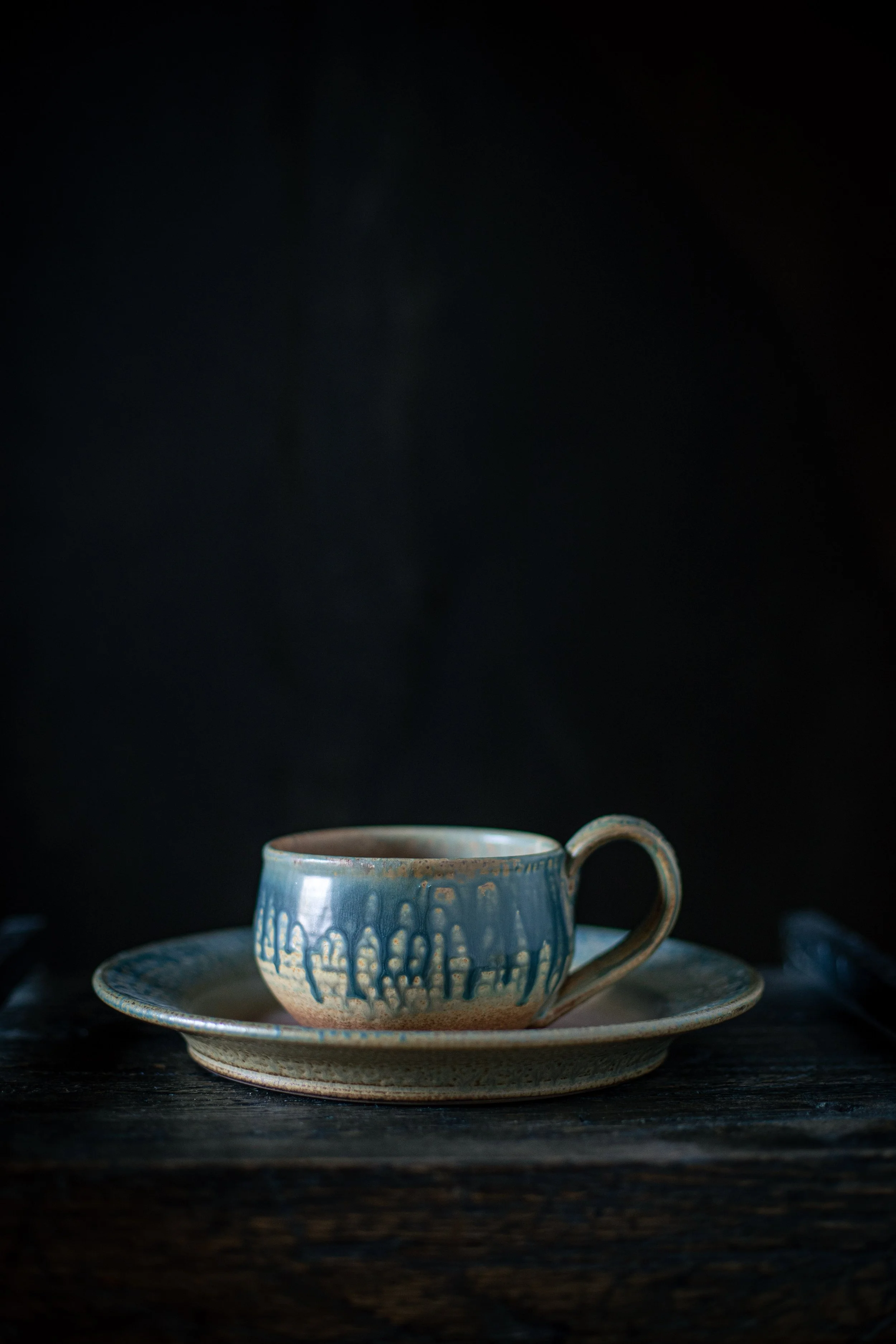 A ceramic cup and a matching saucer on a dark wooden surface, with a dark background.