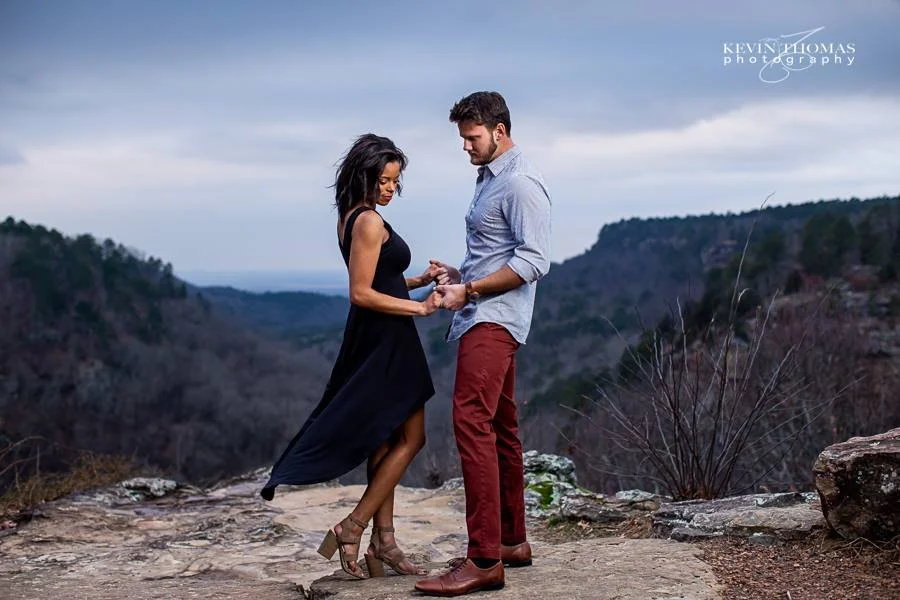 A couple dancing on a rocky overlook with a mountain landscape in the background.