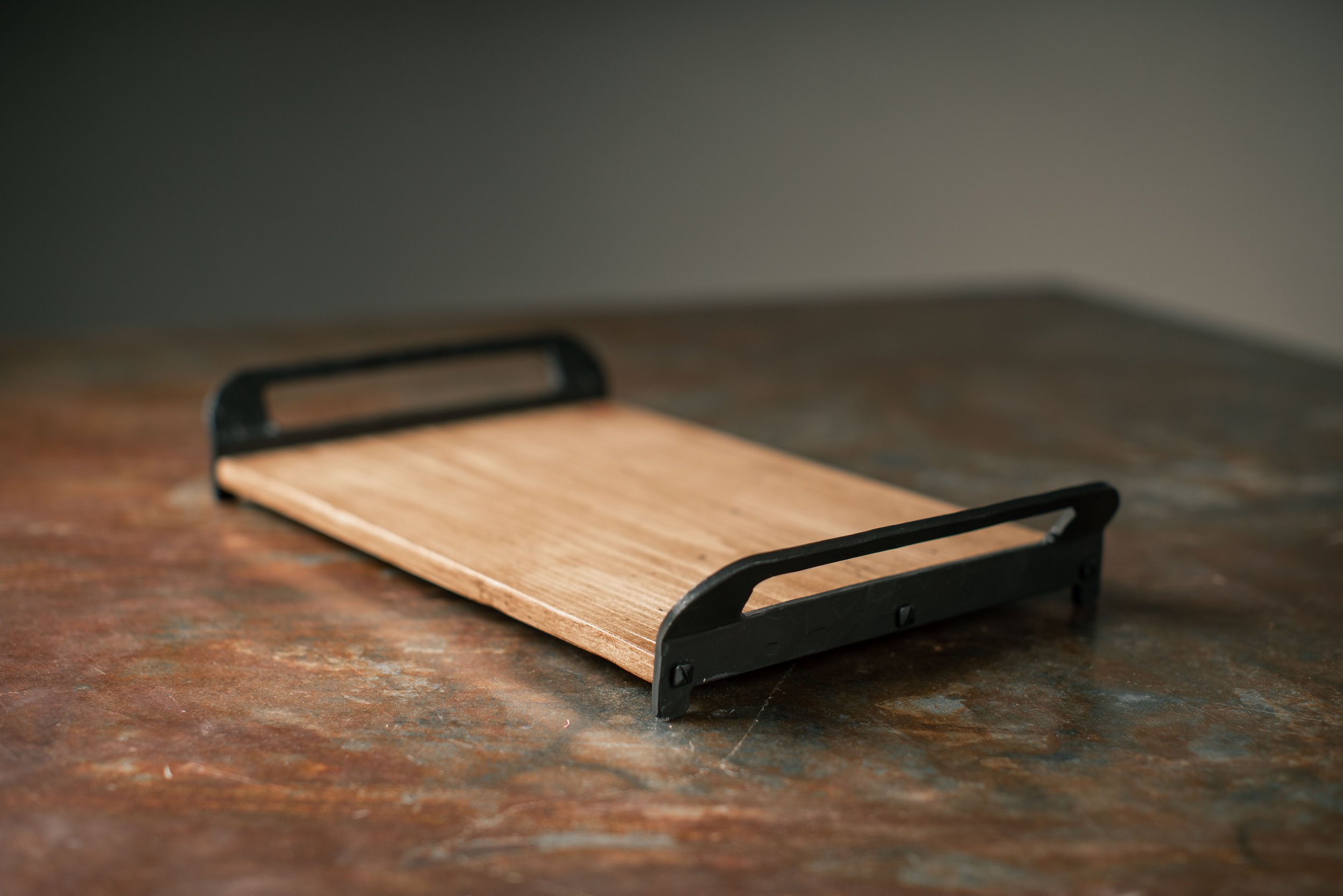 A small wooden serving tray with black metal handles on a wooden surface.