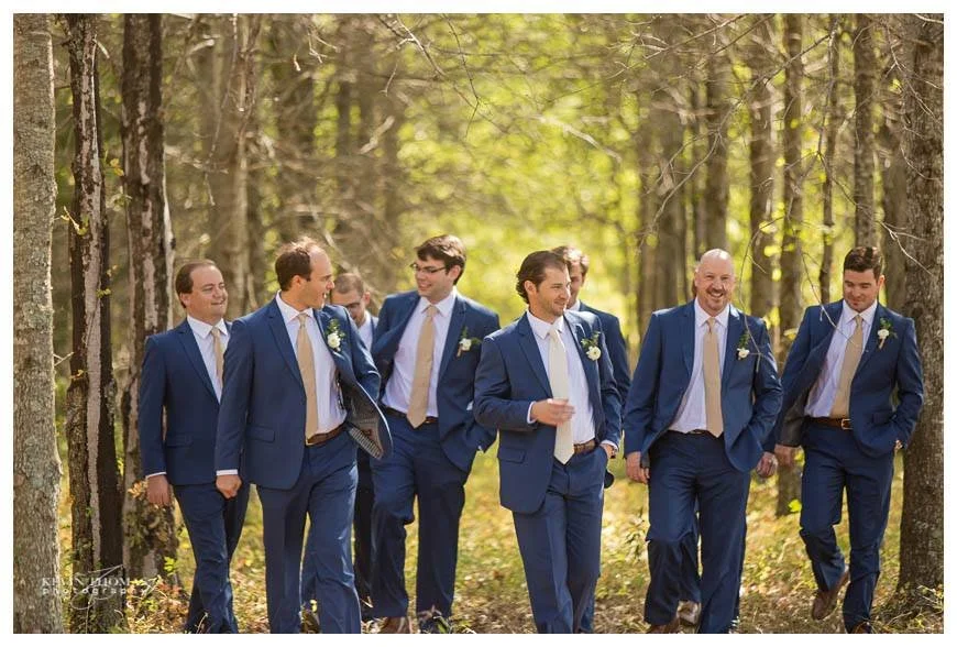 Group of men in blue suits walking through a forest during daytime, smiling and chatting.