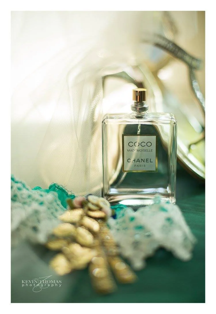 A bottle of Coco Mademoiselle Chanel perfume next to a vintage mirror and some jewelry, with soft natural lighting.