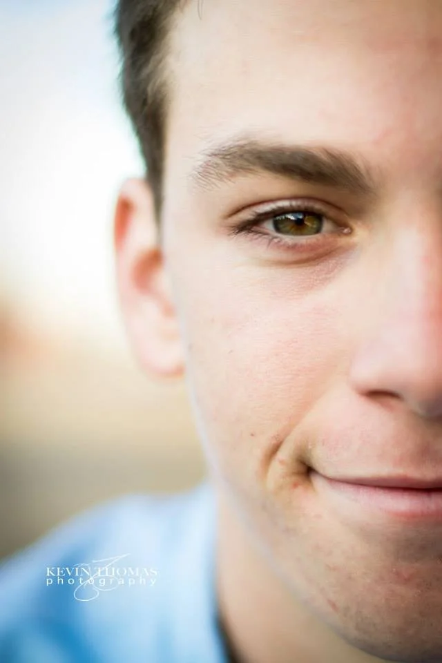 Close-up of a young man's face showing his right eye and part of his mouth, smiling, with light brown hair and fair skin.