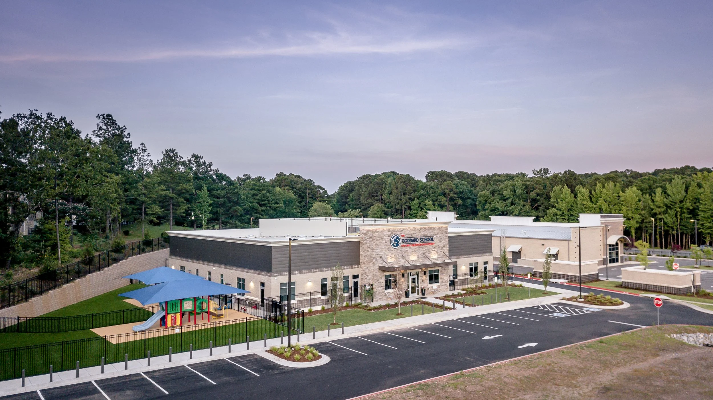 A modern school building with a playground, parking lot, and surrounded by trees and greenery.