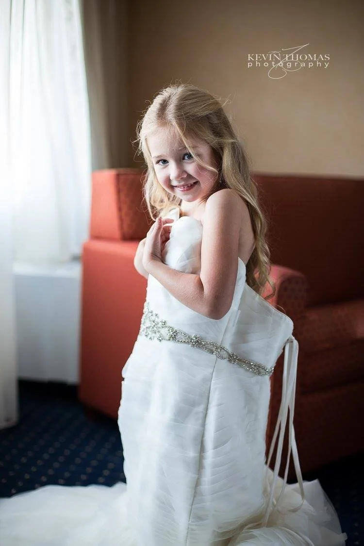A young girl in a wedding dress, smiling and posing indoors.