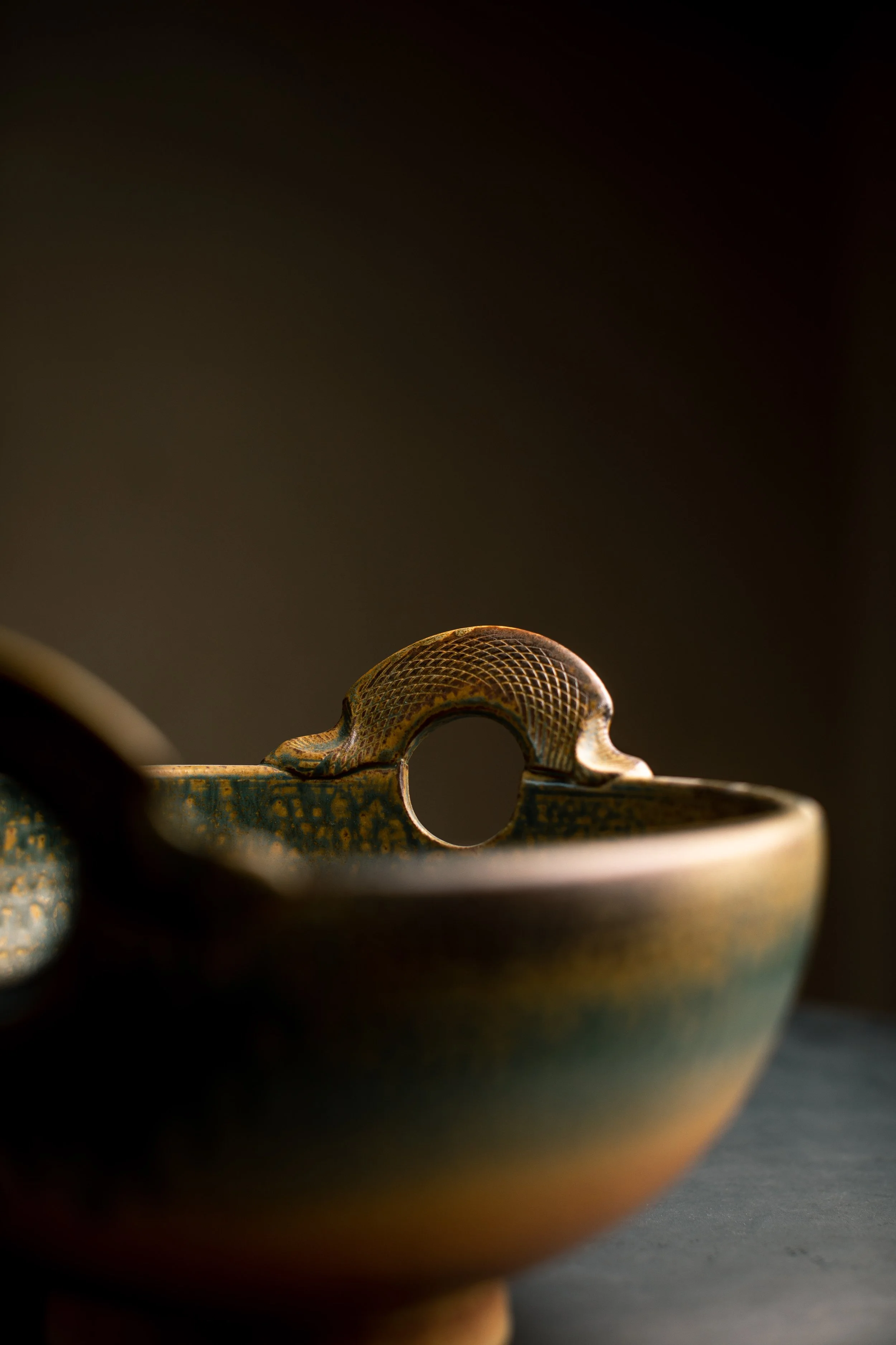 Close-up of a dragon-shaped handle on a ceramic teapot with dark background.