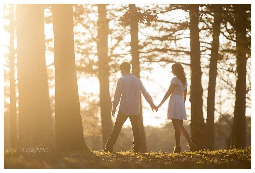 A young couple holding hands in a wooded area during sunset.