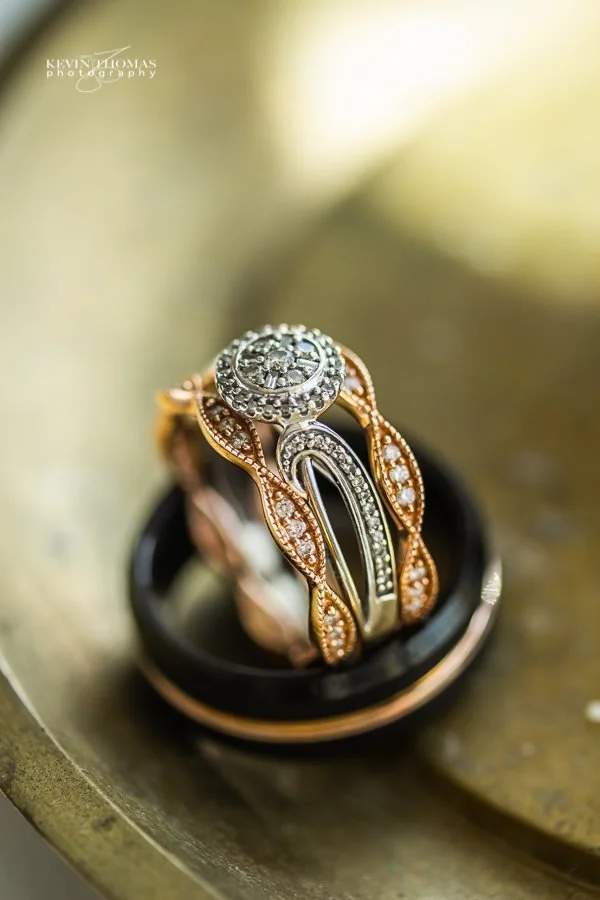 Close-up of layered rose gold and silver rings with diamonds, placed on a dark ring holder, on a textured gold surface.
