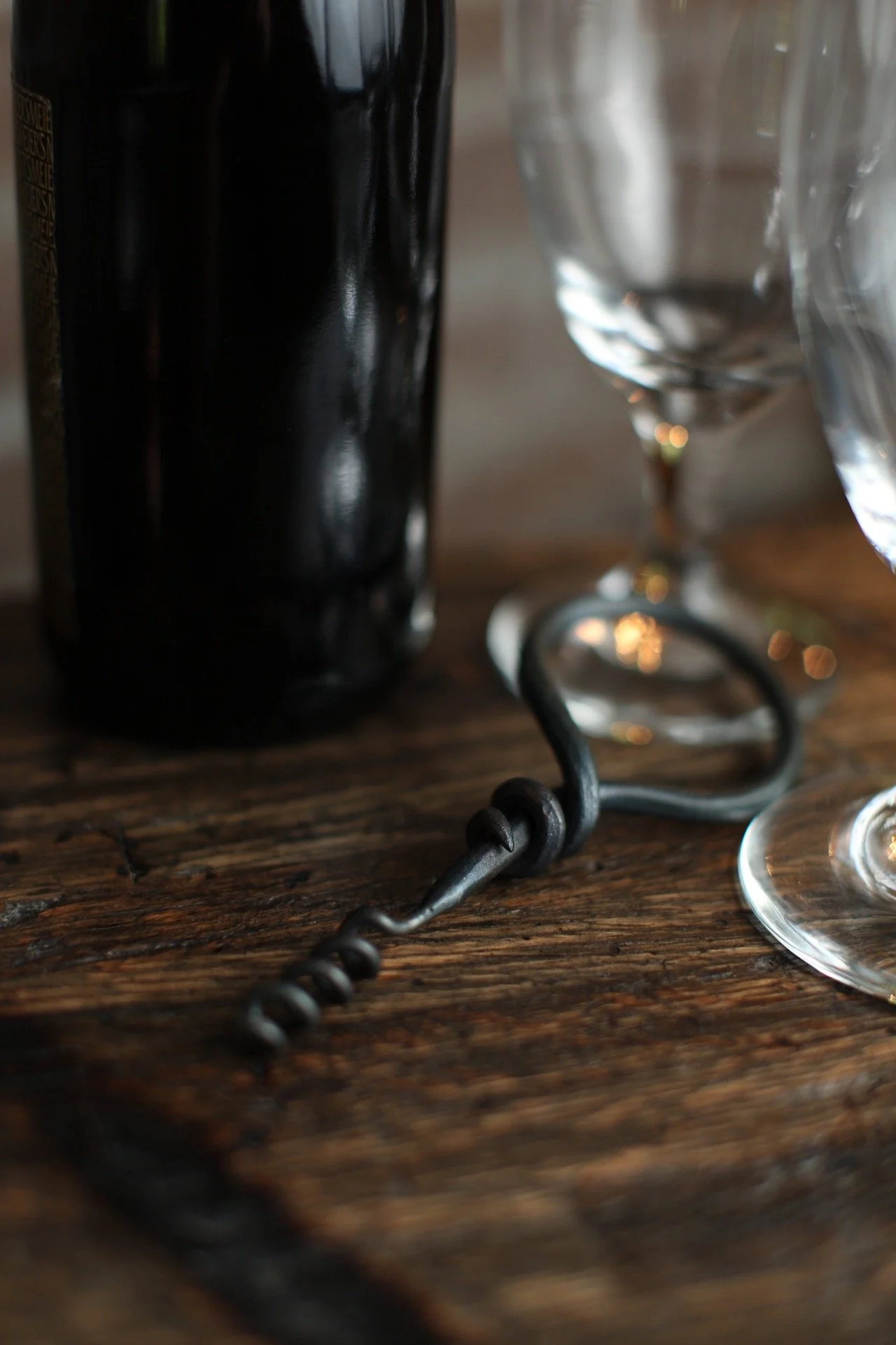 Close-up of a wooden table with a black wine bottle, two empty wine glasses, and a black corkscrew.