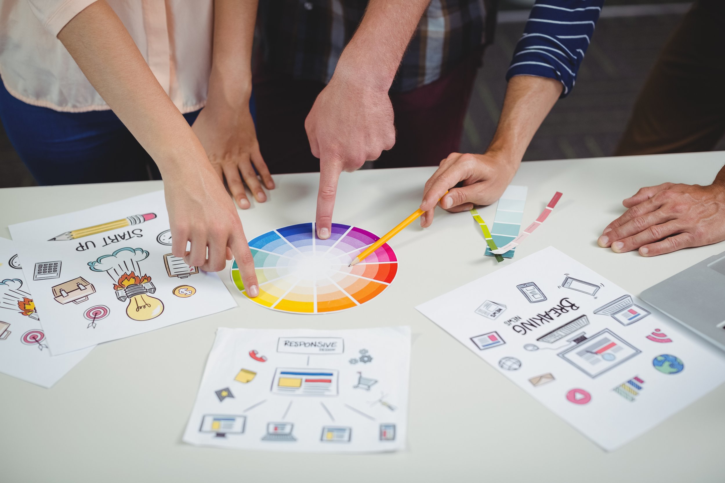 People collaborating around a table with color swatches, printed graphics, and design sketches related to branding and marketing.
