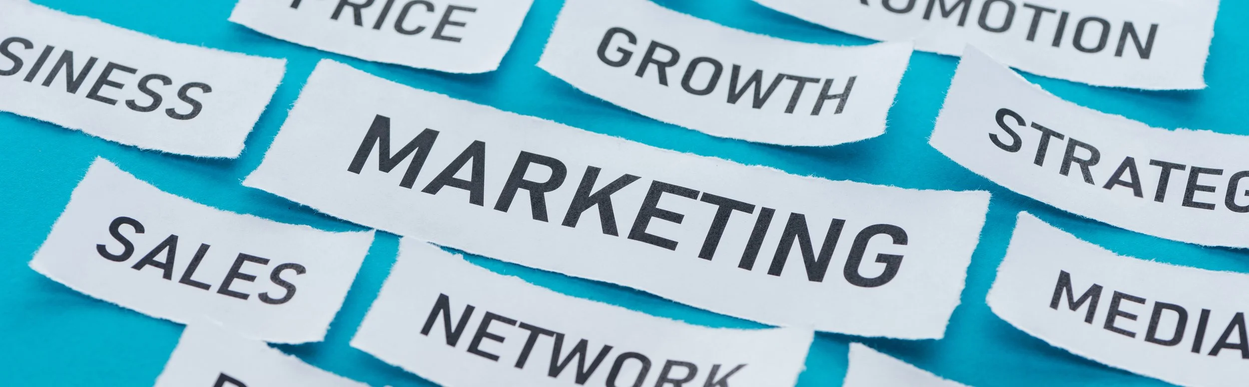 Collage of torn paper pieces with words related to marketing and business, such as 'MARKETING,' 'SALES,' 'GROWTH,' and 'STRATEGY,' arranged on a bright blue background.