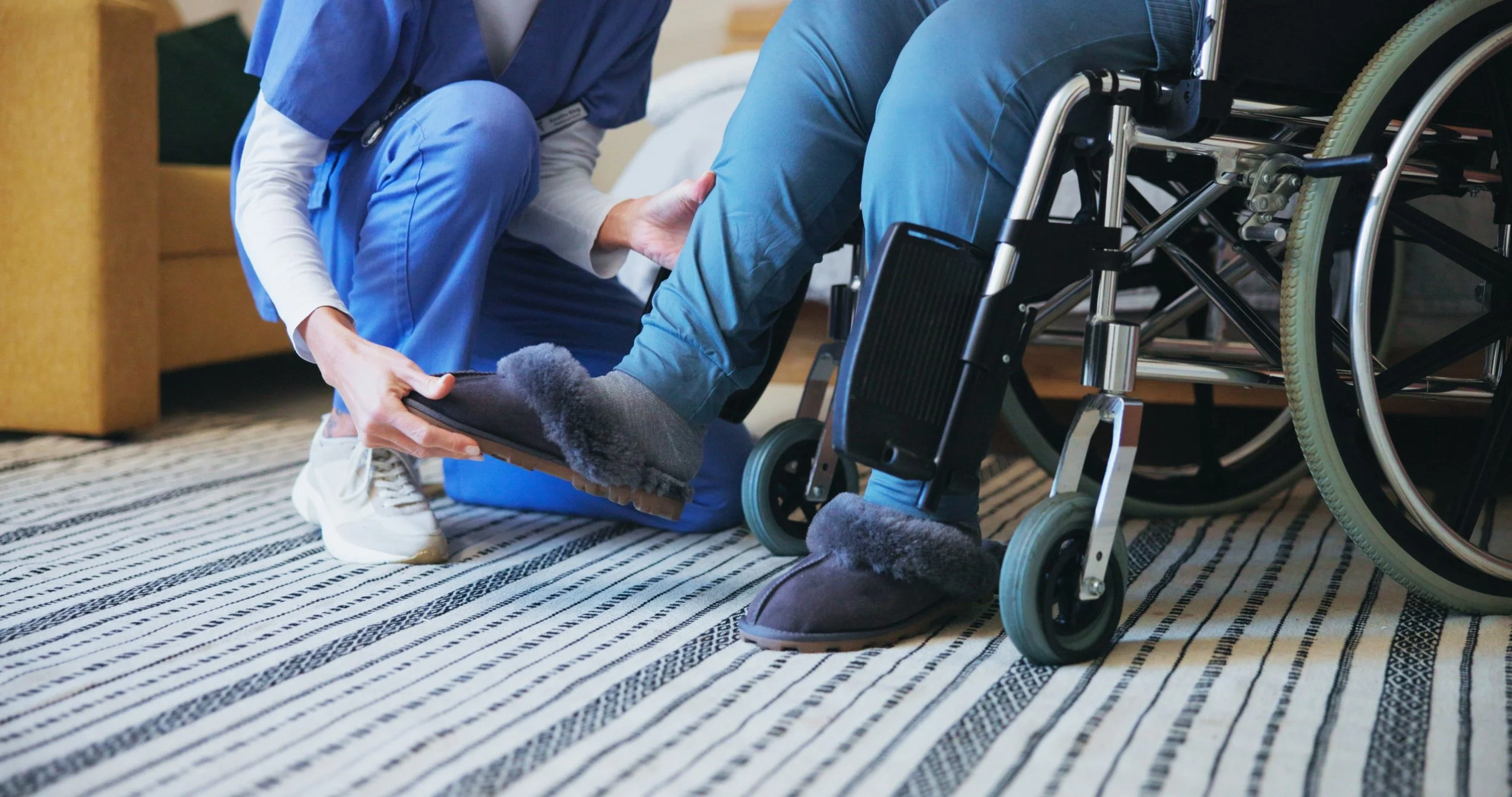 A healthcare worker assisting a person in a wheelchair with footwear at home.