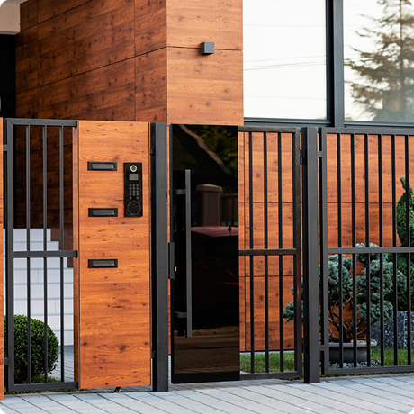 Entrance gate and side wall of a modern house with wooden exterior, black metal gate, and intercom system.