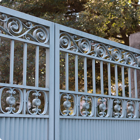Close-up of a decorative metal gate with scrollwork and circular accents, set against trees and sky in the background.