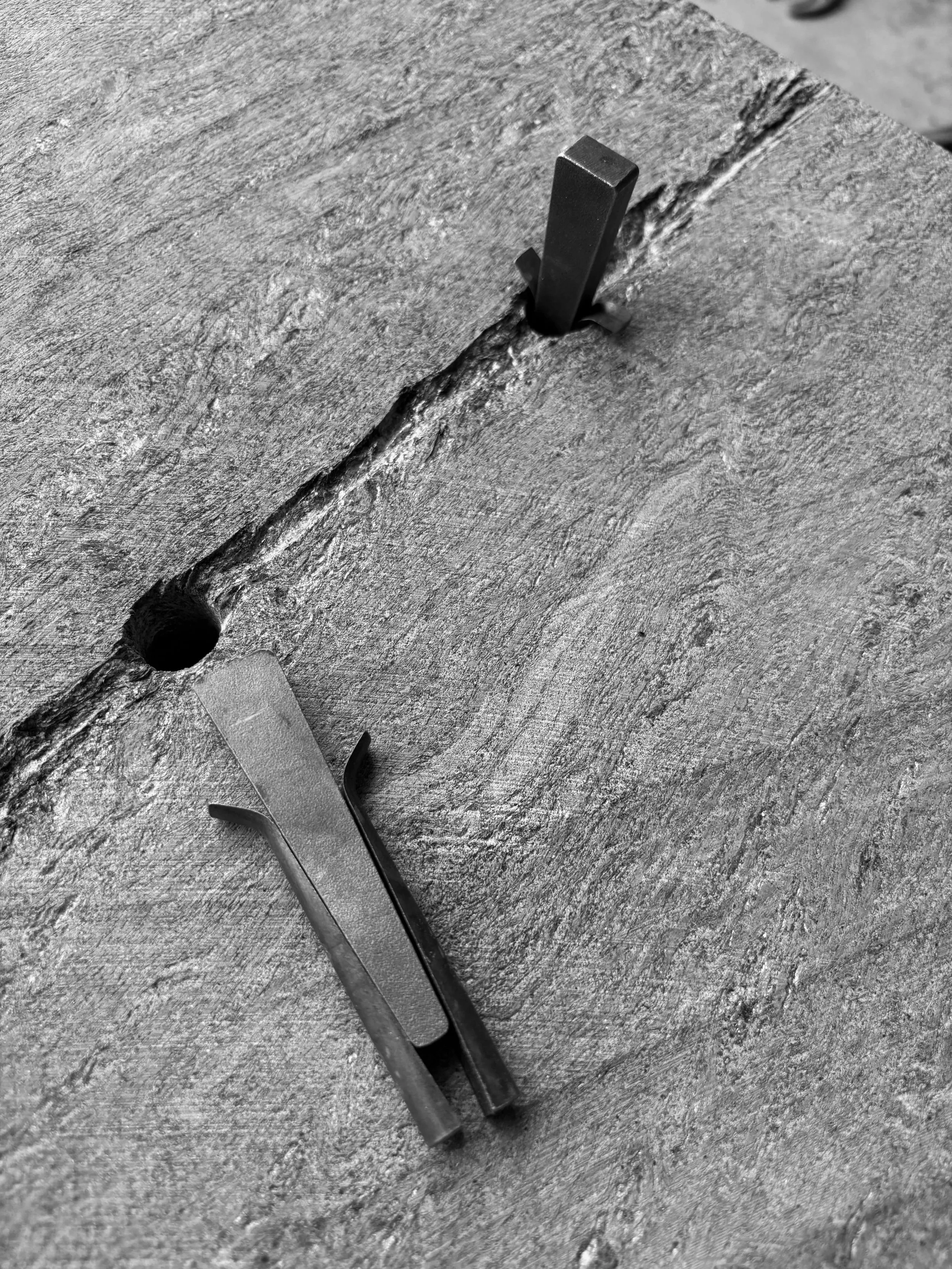 Close-up of a textured wooden surface with two metal hooks inserted into a crack.
