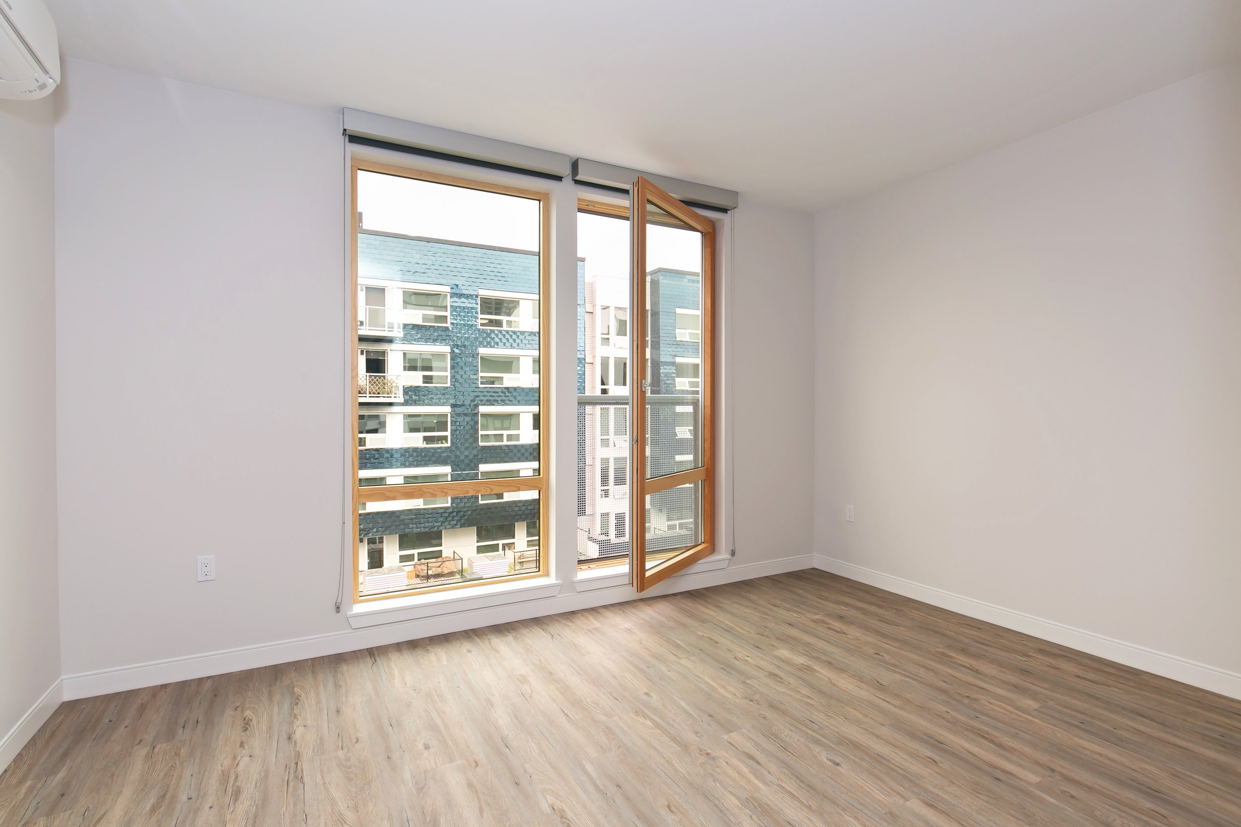 Empty room with large window and wooden floors.