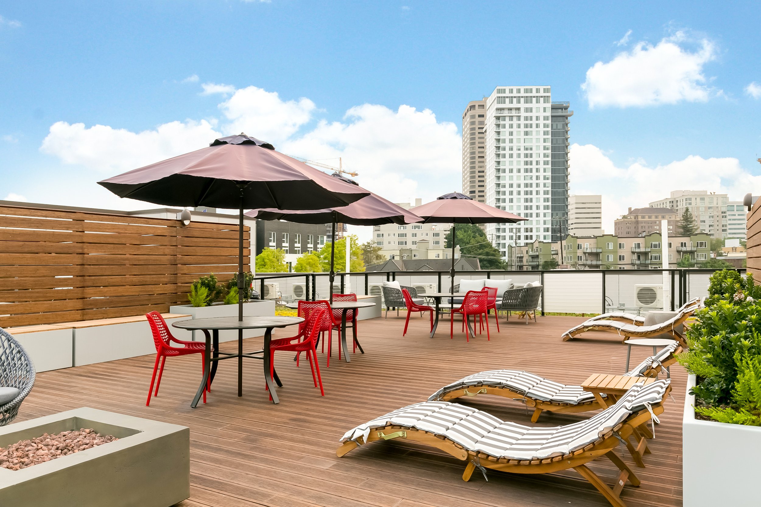 Rooftop patio with lounge chairs, tables with umbrellas, and city skyline in the background.