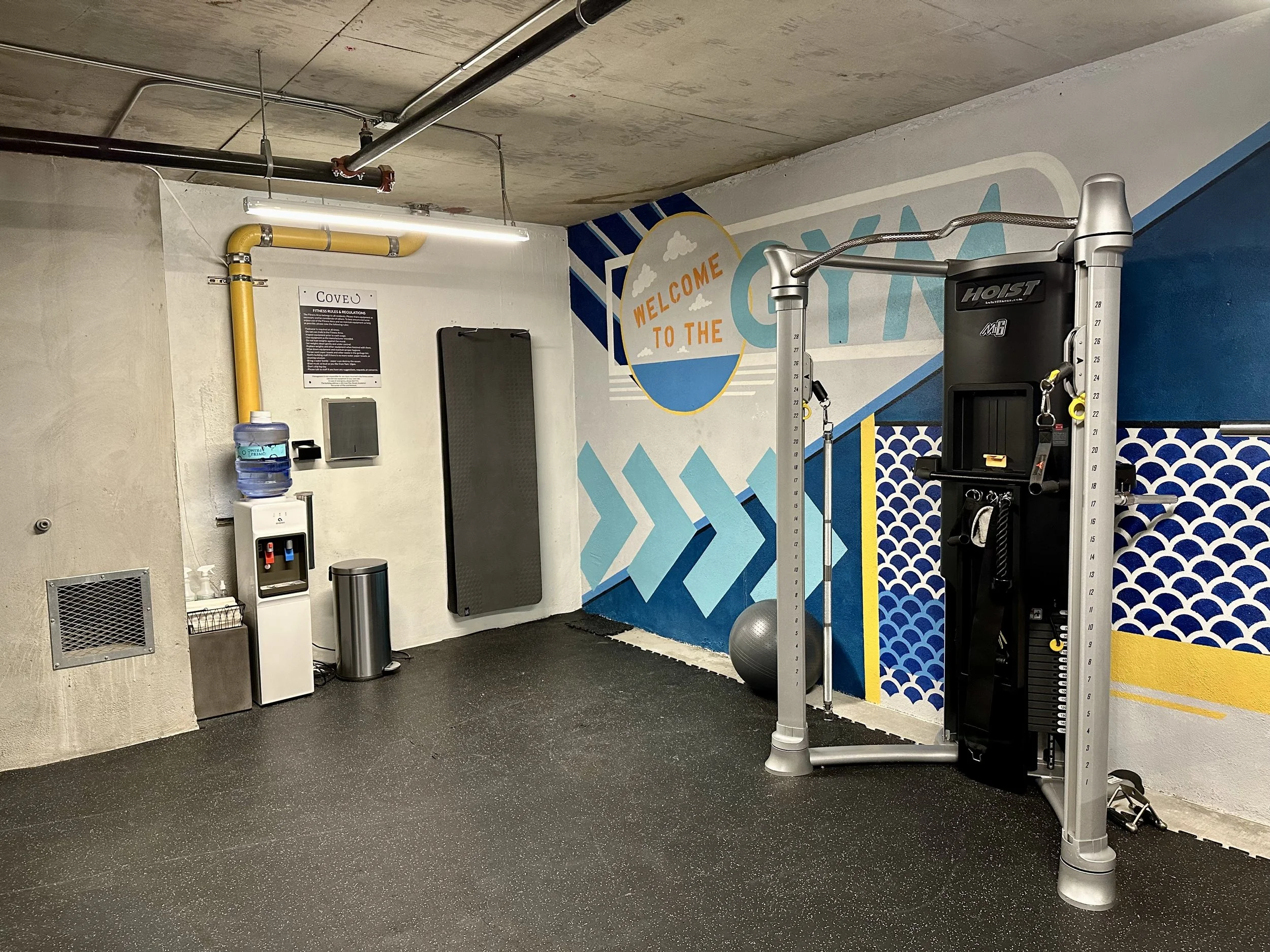 The fitness center of the Cove apartments on Capitol Hill in Seattle, Washington featuring a cable machine, yoga mats, and a water dispenser.