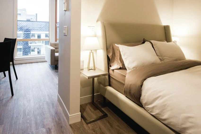 Hotel room with a bed, bedside table with a lamp, and a sitting area with a chair and window