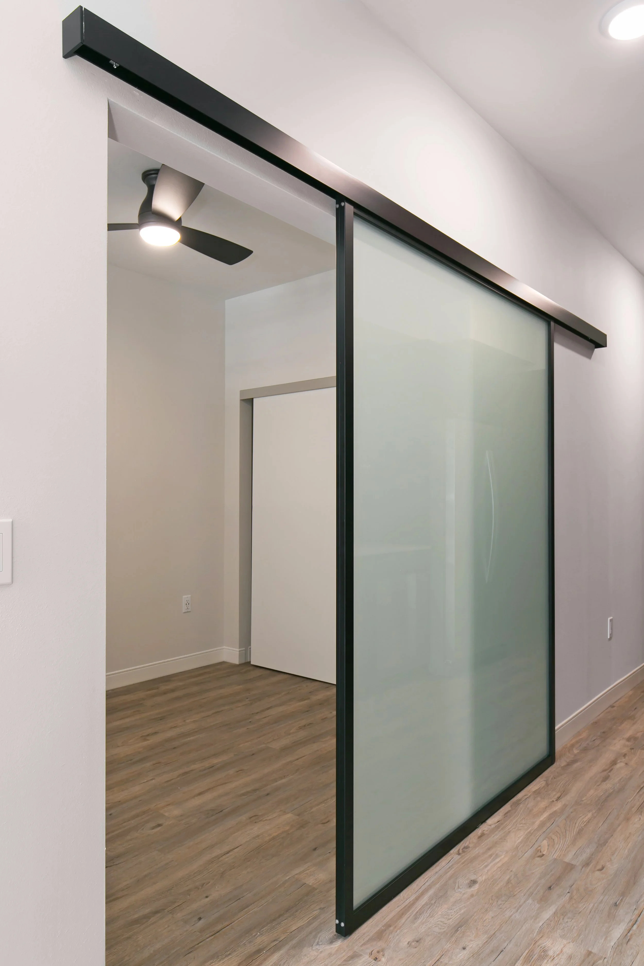 A modern interior room with a sliding glass door with black frame, a ceiling fan, and wood flooring.
