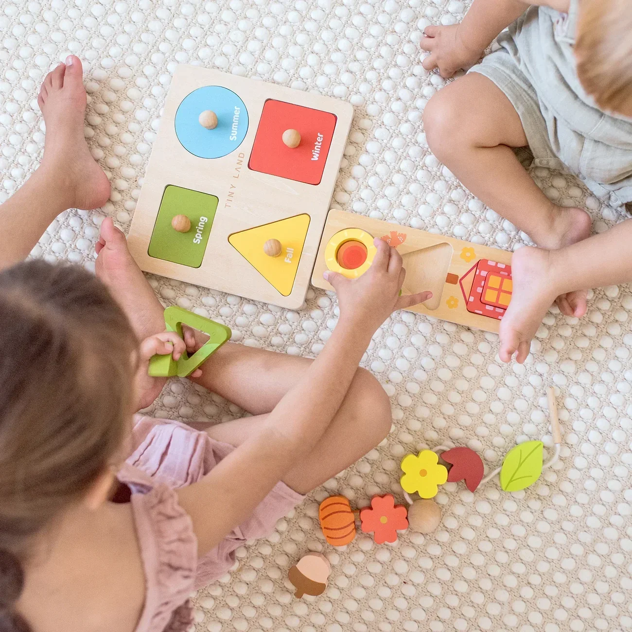 Children playing with a wooden educational puzzle about seasons, with separate pieces representing summer, winter, spring, and fall, on a textured beige surface.