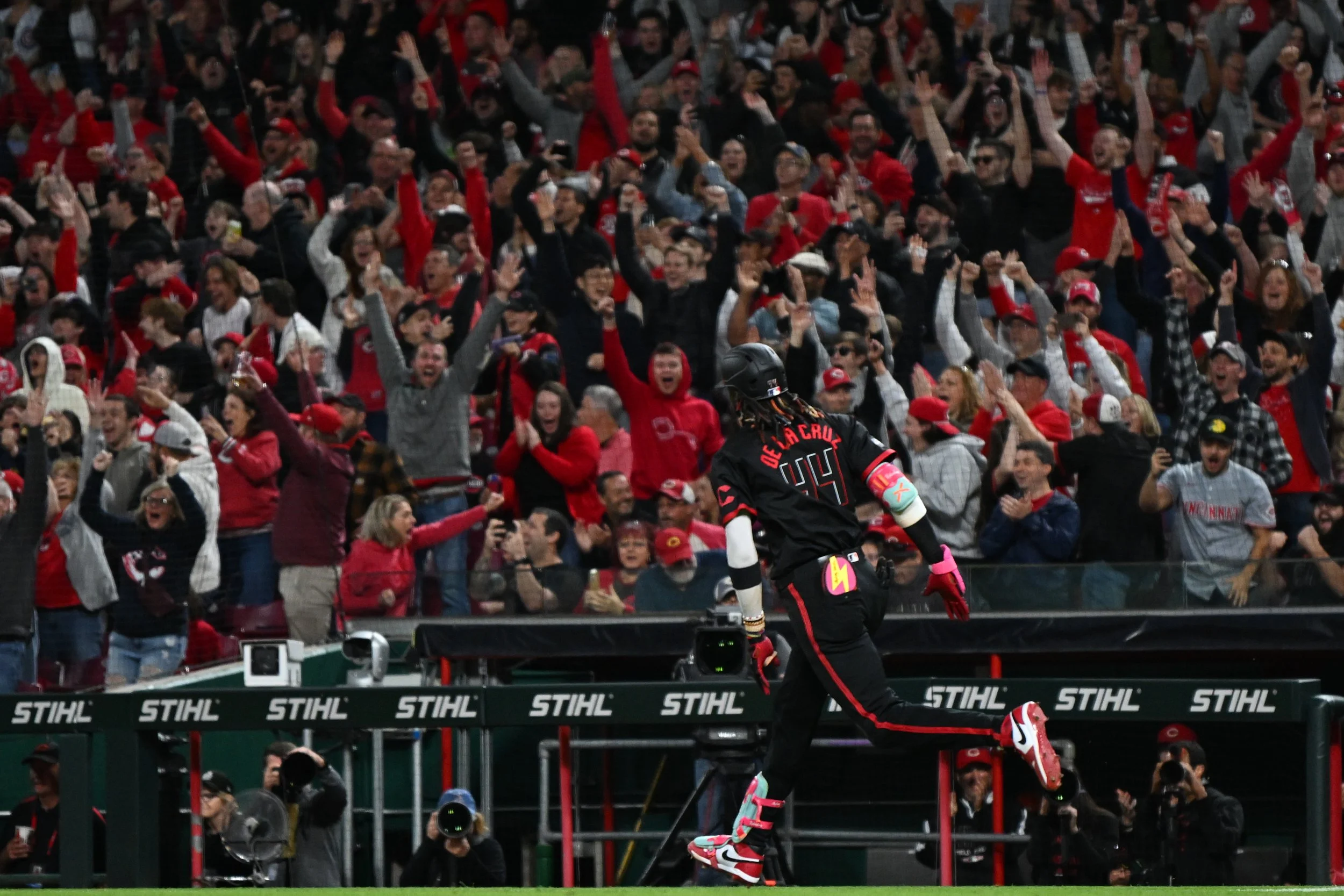 A football player in black uniform with number 14 celebrating on the sidelines as a large crowd of fans wearing red cheer behind him.