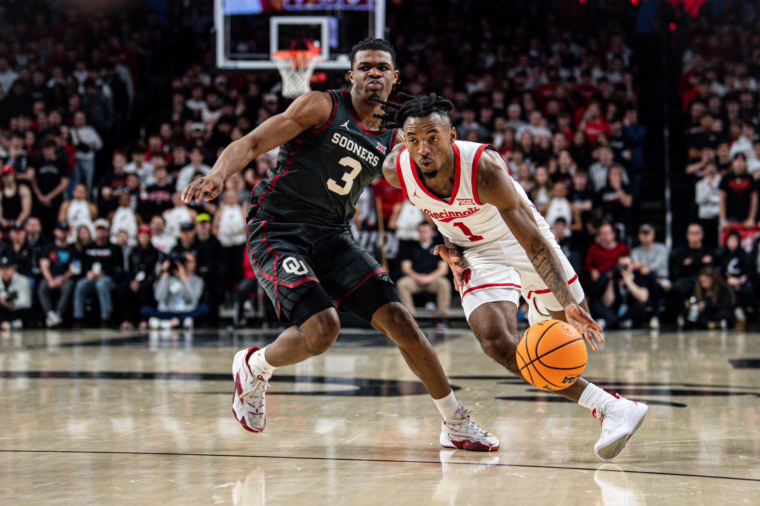 Two basketball players competing for possession of the ball during a game, with a crowd of spectators in the background.