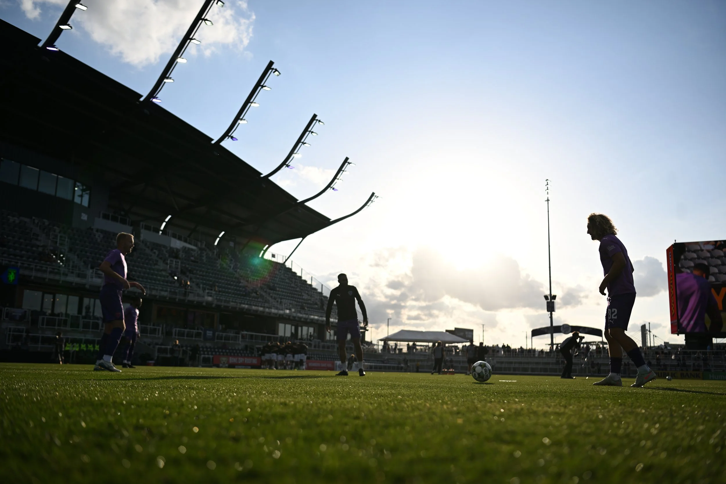 Soccer players warming up on the field at Lynn Family stadium during sunset.